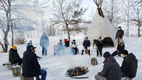 People sitting outside a fire in the wintertime.