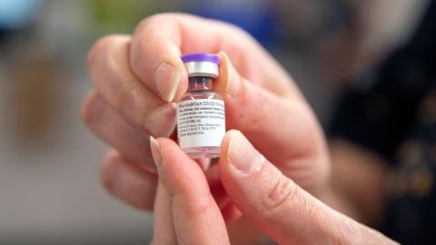 Fingers hold a vial of Pfizer's COVID-19 vaccine