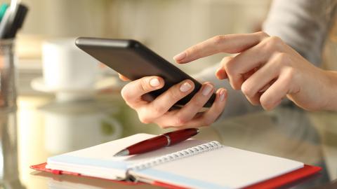 A hand holds a phone overtop of a paper agenda.