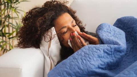 A woman under a blanket blowing her nose