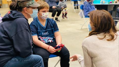 A parent and child at a vaccination clinic speak with a staff member.