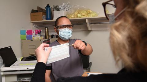 A health-care worker hands a person a medical mask.