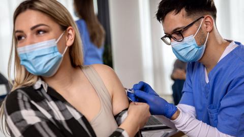 Health-care provider injects a needle of vaccine into arm of a female patient.