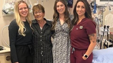 Three health-care providers stand alongside a patient in a hospital room.