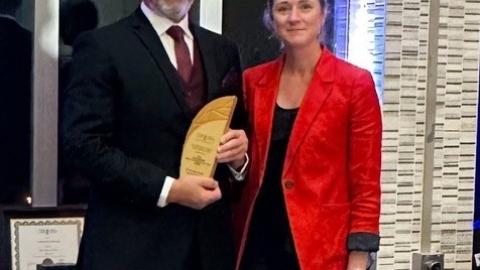 Dr. Schalk Van der Merwe and President of Saskatchewan College of Family Physicians, Dr. Darcie McGonigle pose together, at an award ceremony. Both are dressed formally and Dr. Van der Merwe holds an award for the 2024 Family Physician of the Year – Saskatchewan.