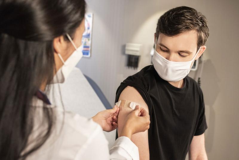 A band-aid is placed on the arm of a young man by a medical professional.