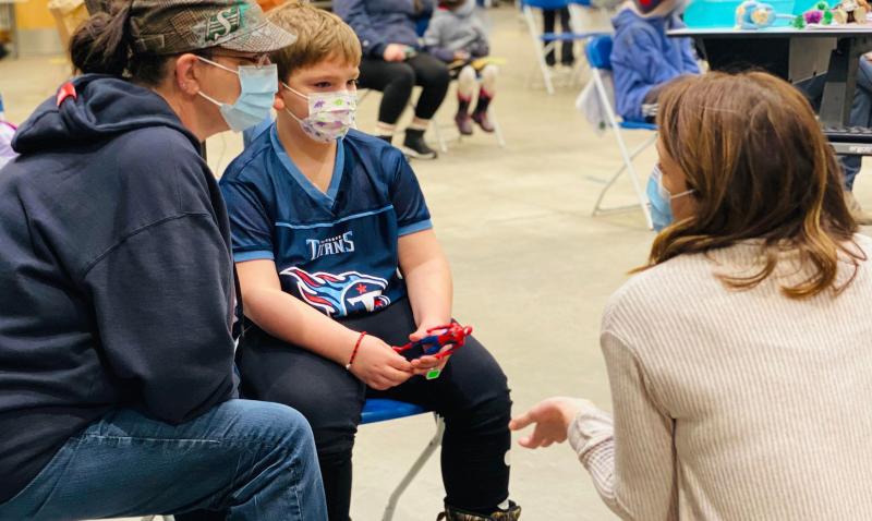 A parent and child at a vaccination clinic speak with a staff member.