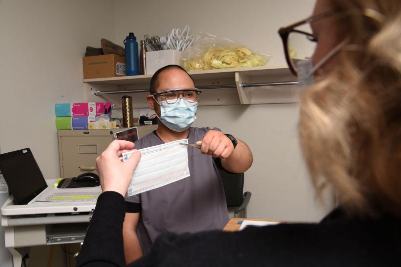 A health-care worker hands a person a medical mask.