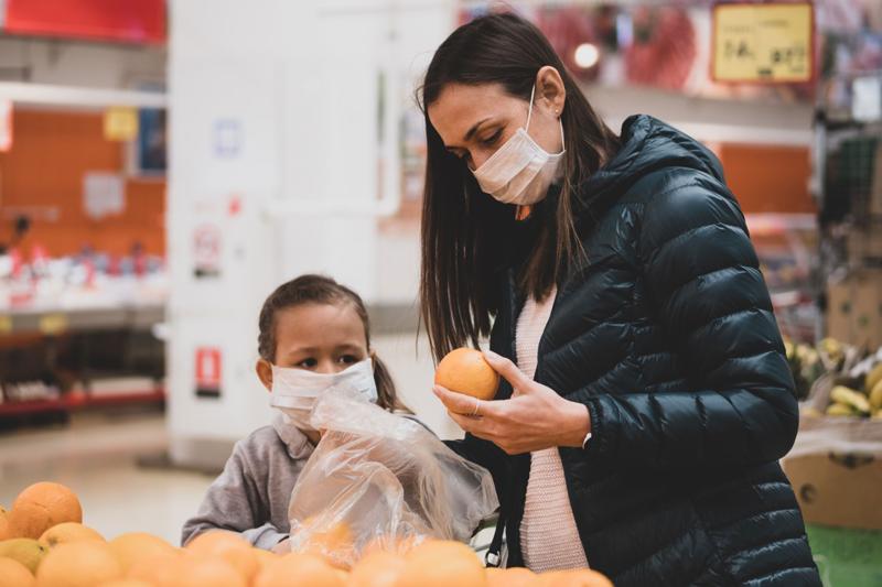 A mother and daughter wear masks while shopping for groceries.