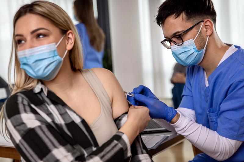 Health-care provider injects a needle of vaccine into arm of a female patient.