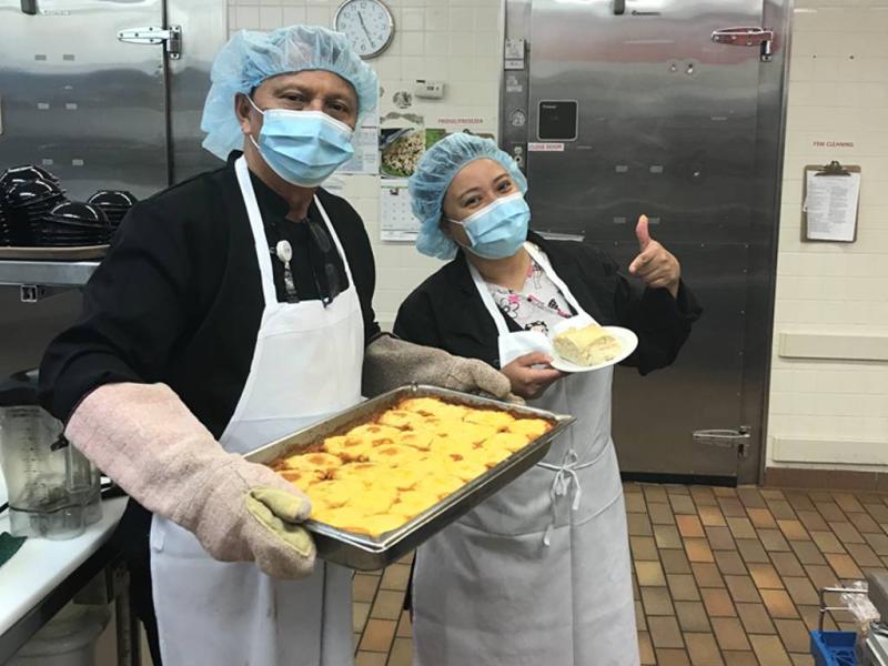 A cook and his coworker pose with a pan of food.
