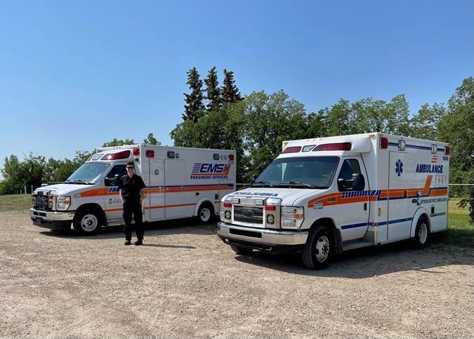 Denys Kotelnikov, a Primary Care Paramedic, stands in front of two ambulances.