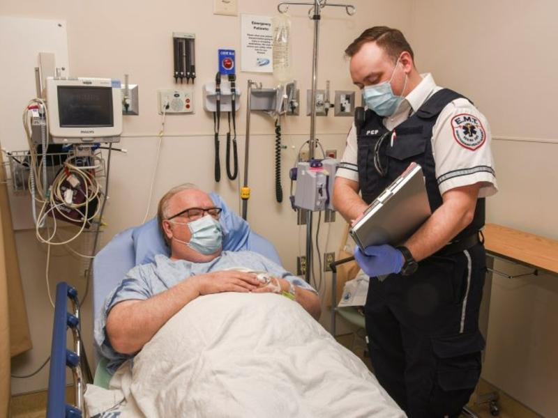 An EMS worker talks to a patient while standing at their bedside.