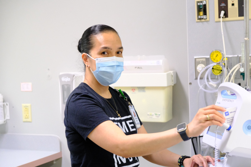 A Registered Nurse wears a mask in a hospital room.