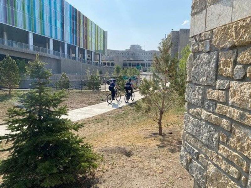 Two Protective Services Bike Officers are seen cycling across a courtyard. 