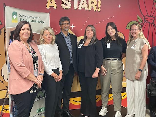 Six health care professionals link arms in professional outfits at a media event at Jim Pattison Children's Hospital in Saskatoon