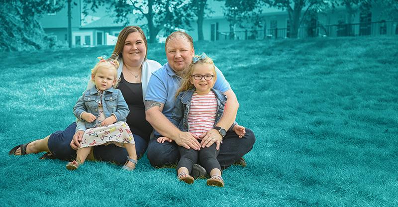 Family with parents and two children posing in an outdoor space with a teal background