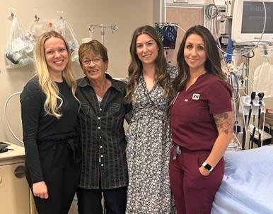 Three health-care providers stand alongside a patient in a hospital room.