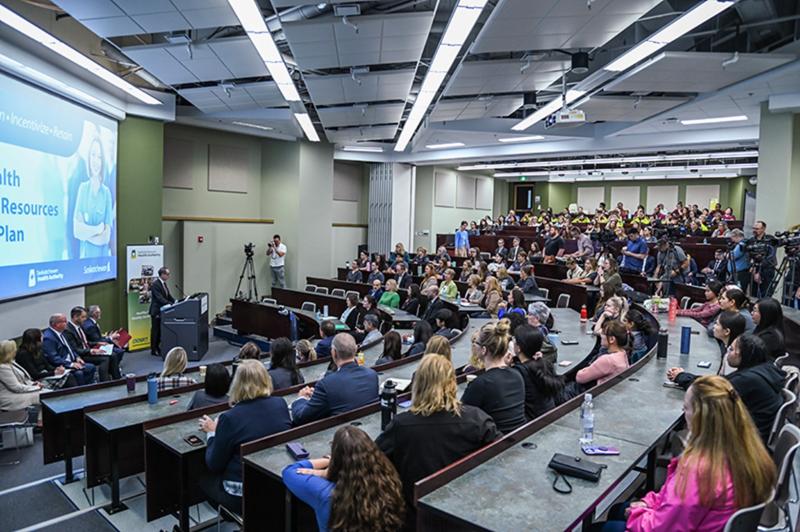 People seated in an auditorium listening to a speaker