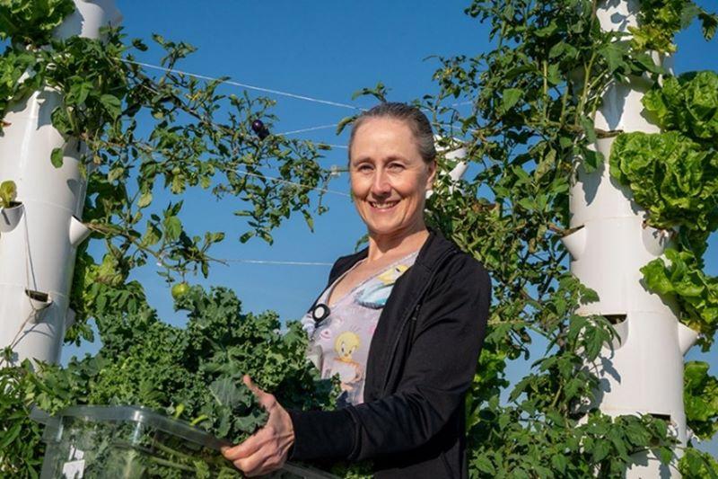 A woman stands holding a container overflowing with freshly picked lettuce