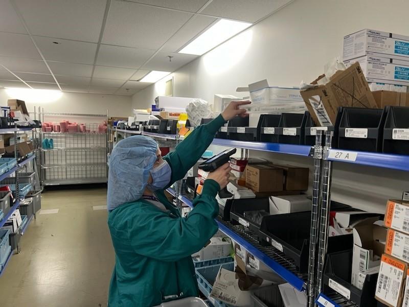 Supervisor grabs an item needed for a cart on the ward. She scans the QR code on the shelf to verify the product before delivery.