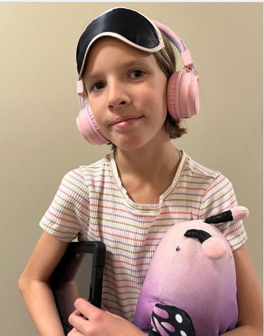 Girl holding a stuffed animal and iPad wearing headphones